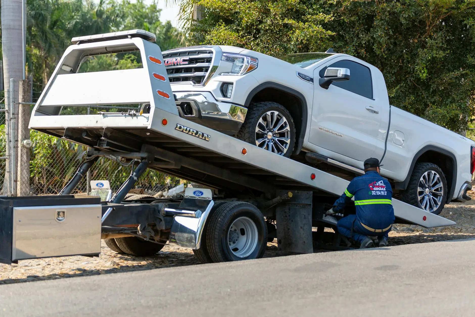A tow truck operator using a wheel-lift to safely recover a vehicle from a tight parking spot in a Malden residential neighborhood.